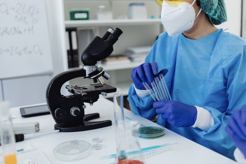 Uma cientista num laboratório a segurar em tubos de ensaio em frente a um microscópio