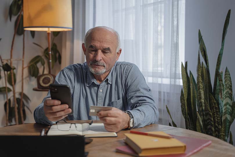 Um homem idoso a usar um telemóvel enquanto segura um cartão de crédito