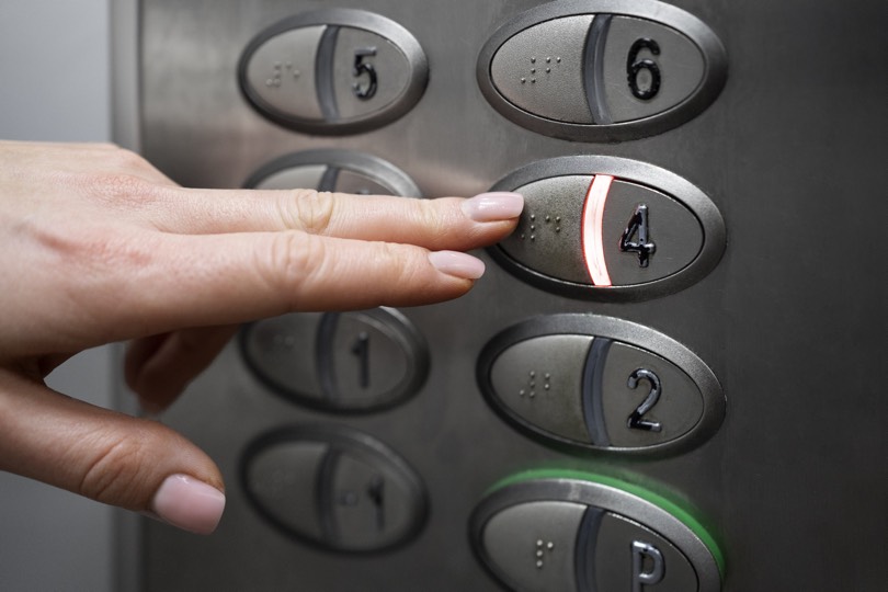 Pessoa cega a carregar no botão do elevador em Braille.